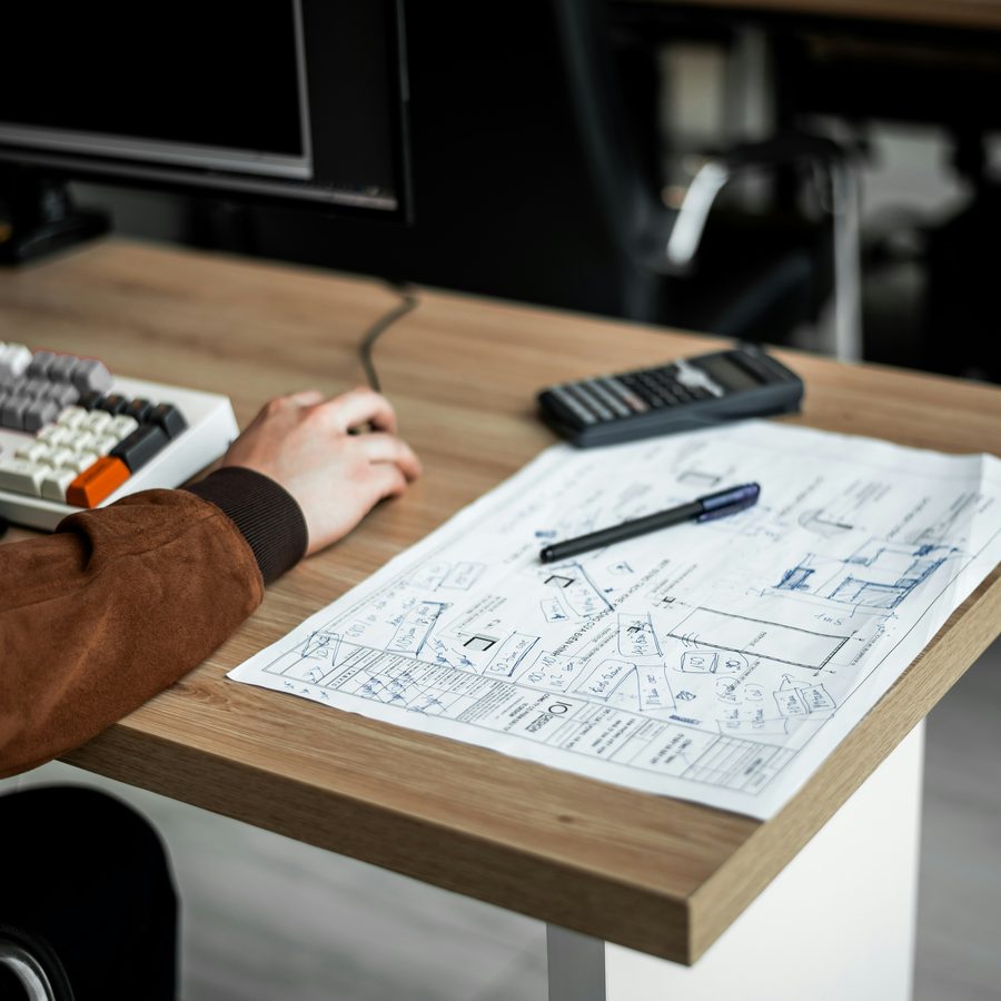 Sourcing agent checking a technical drawing and calculator draft on a desk
